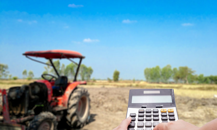 A calculator and the blur farm and tractor in background as a farmer works on agriculture accounting.