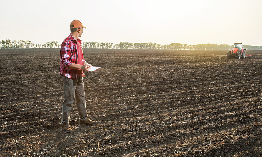 Farmer man with notebook in field with tractor, calculating farm income taxes.