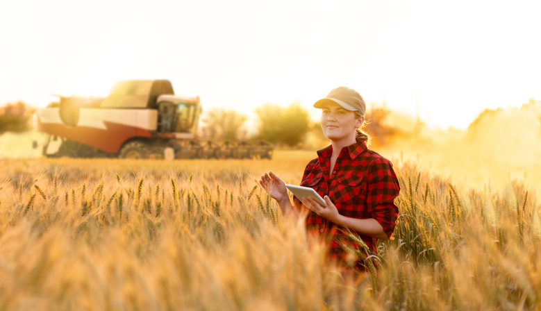 A farmer with digital tablet controls an autonomous harvester on a smart farm, reading about financial planning for farmers.